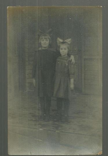 REAL PHOTO POSTCARD OF TWO YOUNG GIRLS ON PORCH WITH LARGE HAIR BOWS
